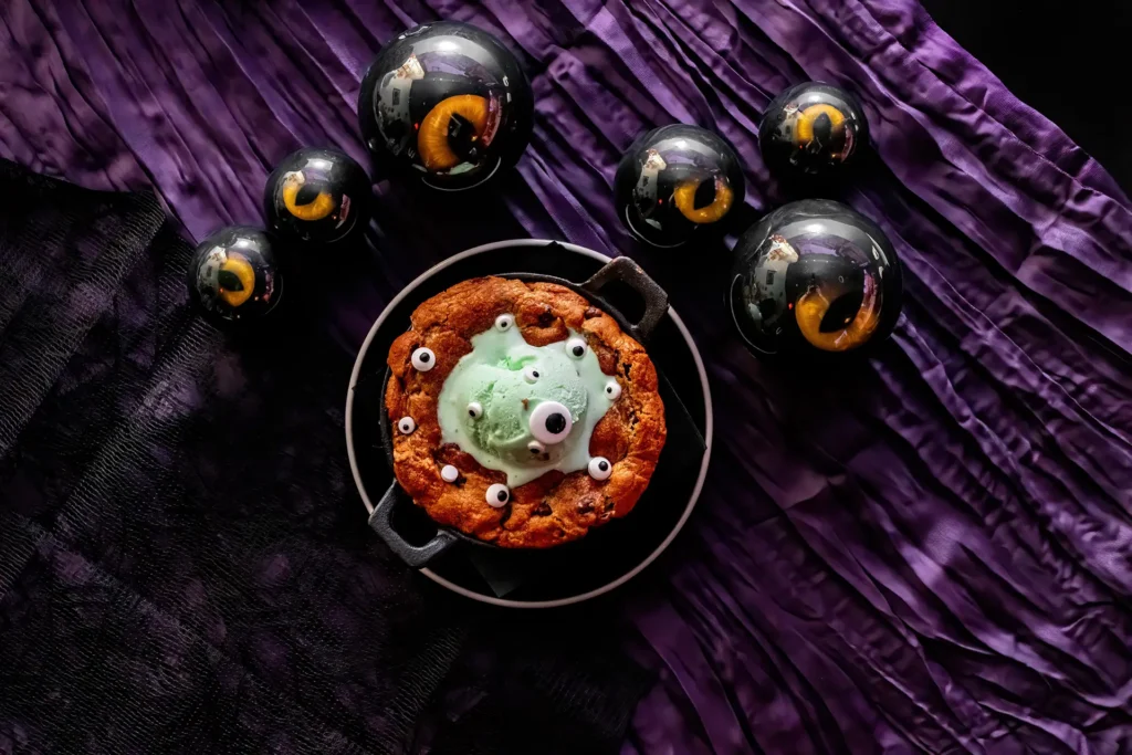 Overhead view of the Monster Cookie Skillet with green ice cream and candy eyeballs surrounded by Halloween decorations.