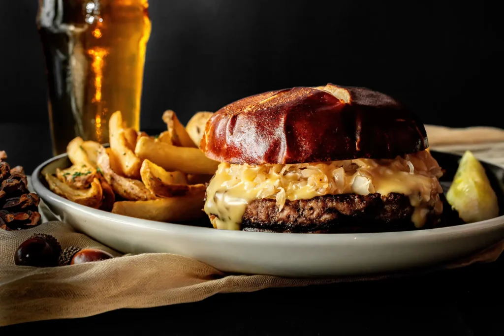 Oktoberfest Burger topped with beer cheese sauce and sauerkraut on a pretzel bun, served with seasoned potato wedges and a pickle.