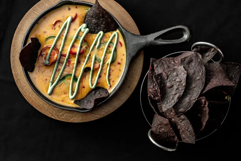 Monster Mash Dip with warm queso, jalapeños and avocado crema, served with dark tortilla chips.